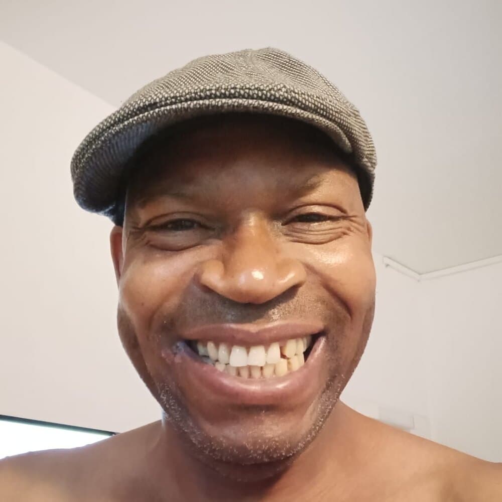Amaechina laughing, wearing a grey flat cap